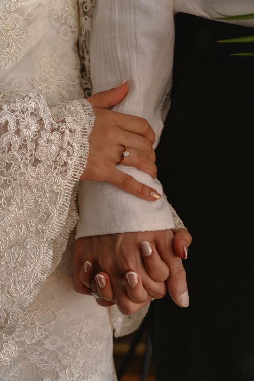Free Intimate close-up of a bride and groom holding hands in wedding attire. Stock Photo