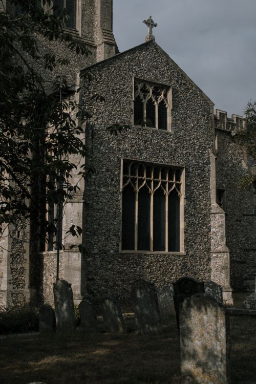 Free Gothic stone church facade in the UK with nearby gravestones on a cloudy day. Stock Photo