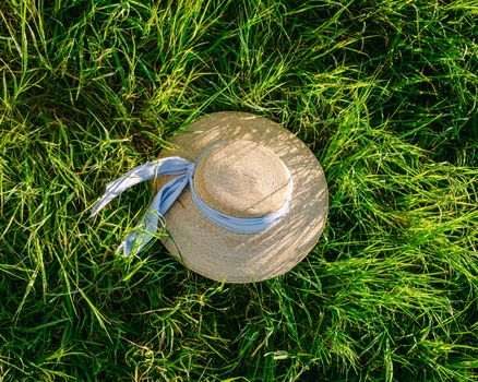Elegant straw sun hat with ribbon resting on lush green grass, capturing a serene summer vibe.