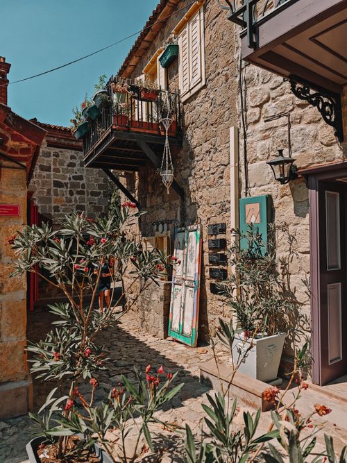 Free Charming rustic stone buildings with balcony and vibrant plants in a sunlit alleyway. Stock Photo