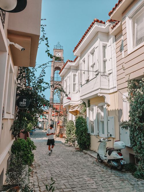 Free Scenic view of a quaint street with a clock tower and lush greenery, capturing a slice of local life. Stock Photo