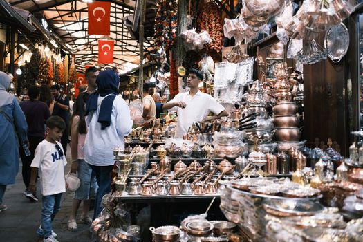 Vibrant market scene showcasing Turkish flags, copper items, and diverse shoppers in an indoor bazaar.
