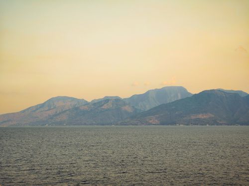 Free Serene view of mountains across the sea at twilight, capturing nature's calm and beauty. Stock Photo