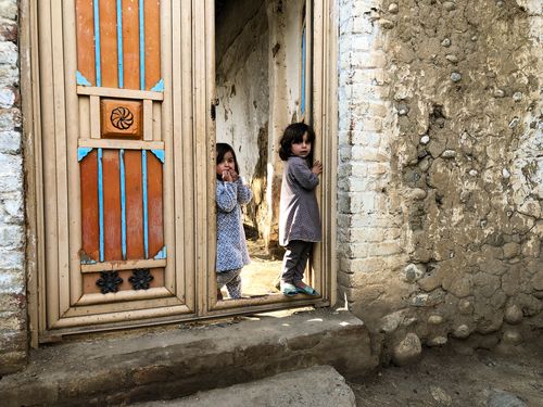 Free Two young girls stand in a doorway of a traditional house in rural Pakistan, exhibiting curiosity. Stock Photo