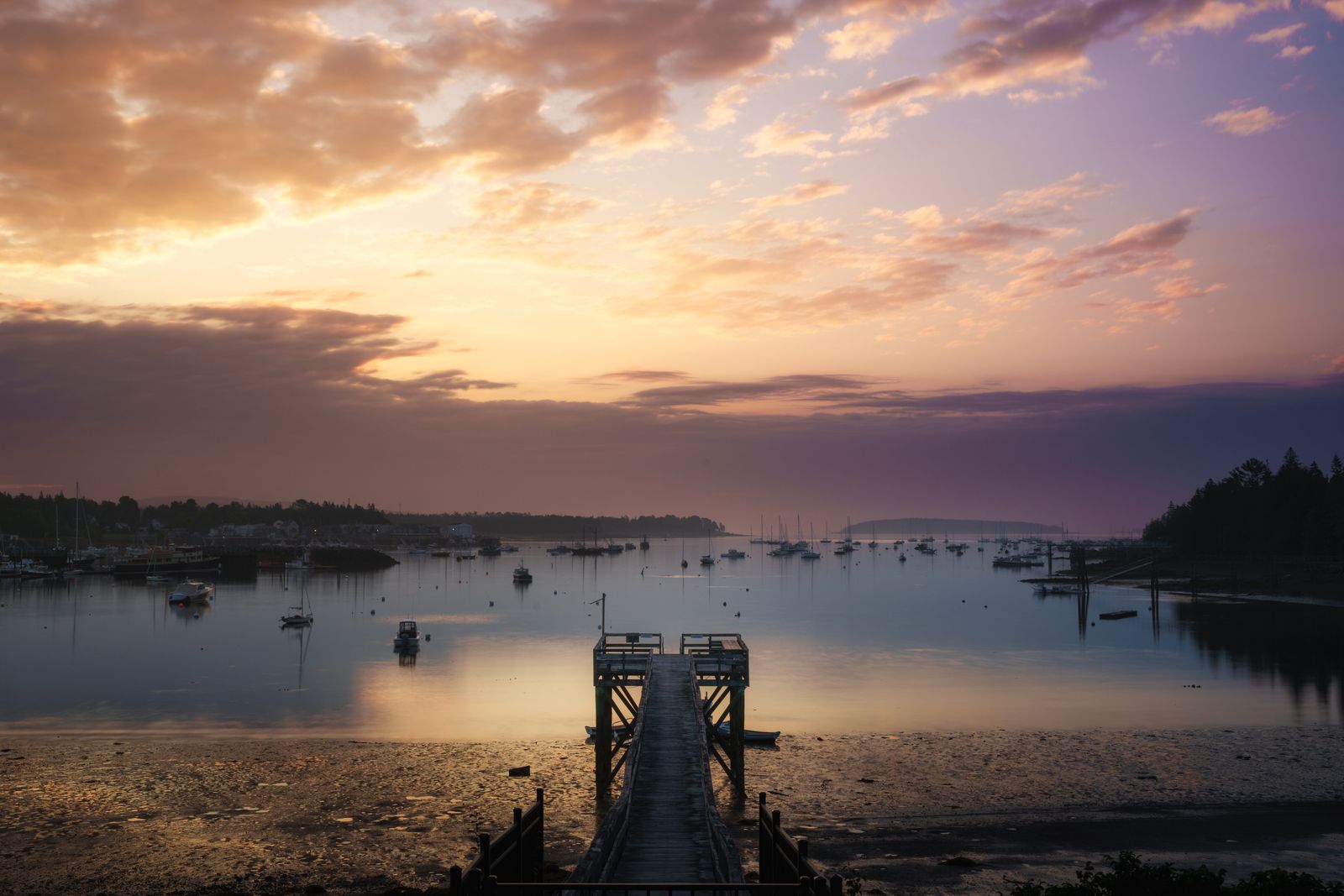 Sunset over a quiet Maine harbor with moored sailboats and a wooden pier