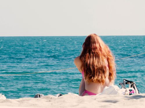 Free A woman enjoys tranquility on a sandy beach with a vast ocean view. Stock Photo