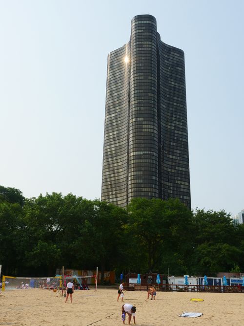 Free A sandy beach in Chicago with people enjoying a sunny day, framed by a modern skyscraper. Stock Photo