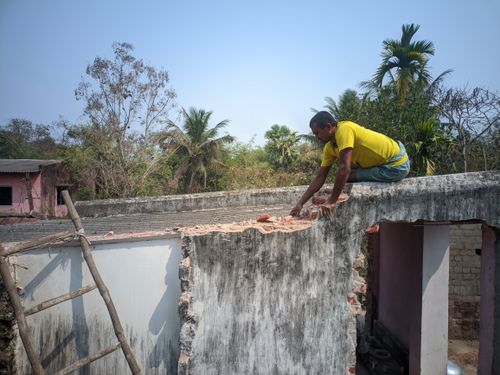 Free A construction worker repairing the rooftop of a building amidst a lush greenery backdrop on a sunny day. Stock Photo