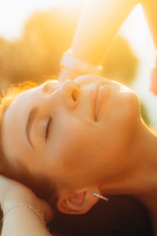 Free A woman enjoys the warm glow of the sunset with a serene expression. Stock Photo