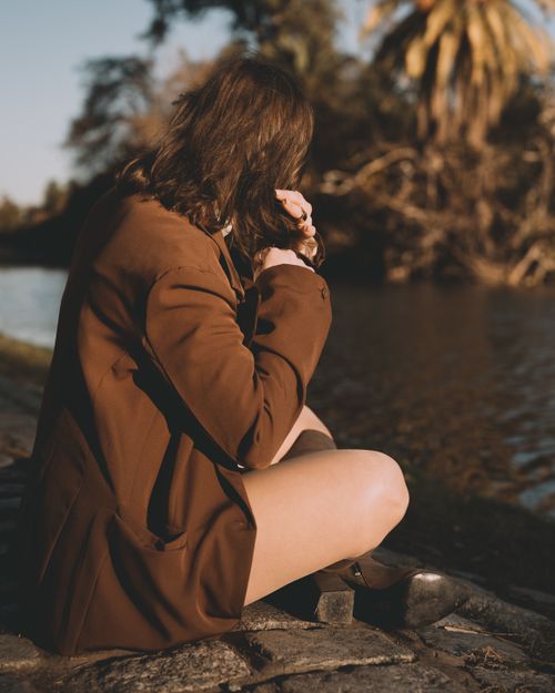 Free A woman seated by a riverbank in Buenos Aires, Argentina, enjoying a peaceful moment outdoors. Stock Photo