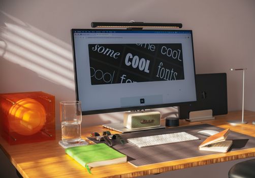 Stylish home office setup featuring a computer, orange lamp, and green notebook in natural light.
