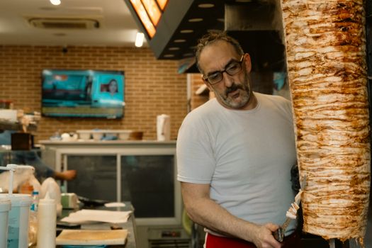 A man skillfully slicing a large kebab in a busy restaurant kitchen, creating delicious shawarma.