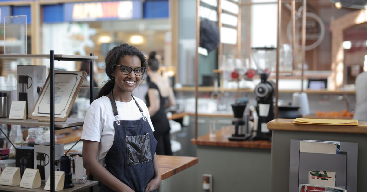 Smiling barista standing in a stylish café, showcasing entrepreneurial spirit.