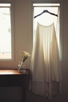 A flowing bridal gown on a hanger by a window with soft natural light.