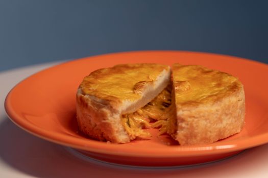 Close-up of a homemade chicken pie sliced open on an orange plate with warm lighting.