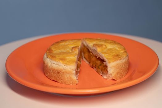 Close-up of a savory pie on an orange plate, cut in half to show filling.