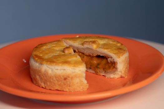 Close-up of a savory pie with a slice removed, served on an orange plate.