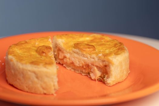 Close-up of a savory pie with a slice removed, on an orange plate.
