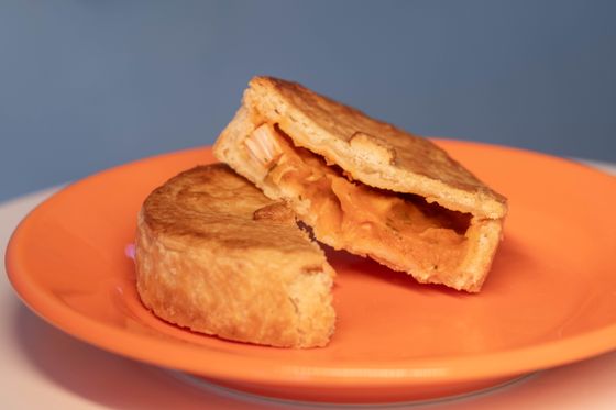 Individual chicken pie cut open showing creamy orange shredded chicken filling on orange plate