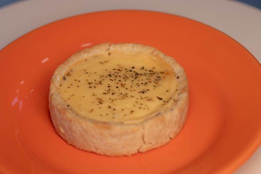 Close-up of a creamy cheese tart garnished with herbs on an orange plate.