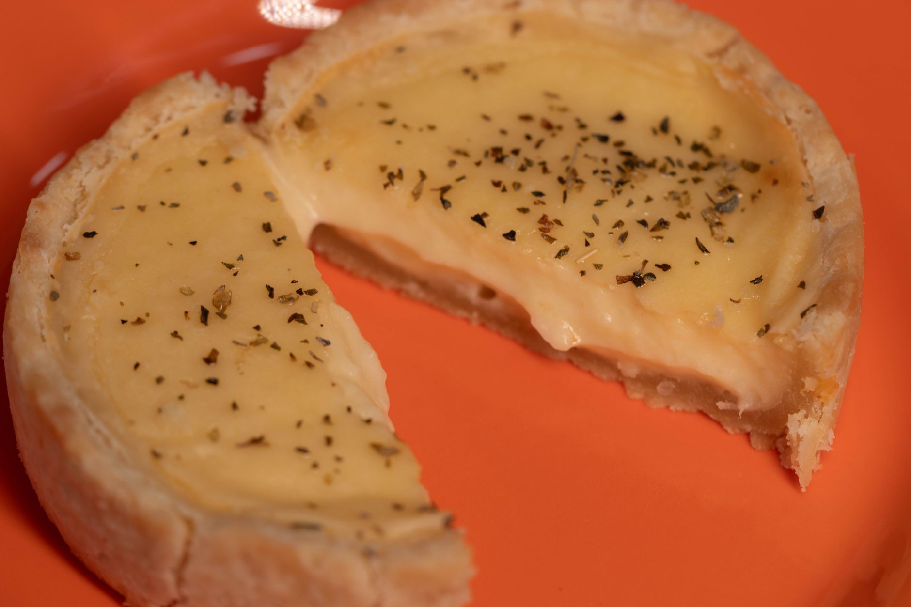 A savory cheese tart sliced in half, garnished with herbs, on a vibrant orange plate.