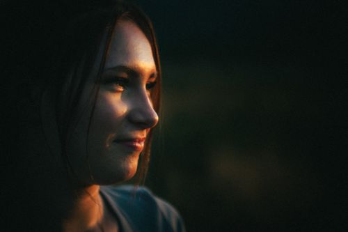Free A serene portrait of a woman enveloped in warm evening light, creating a moody atmosphere. Stock Photo