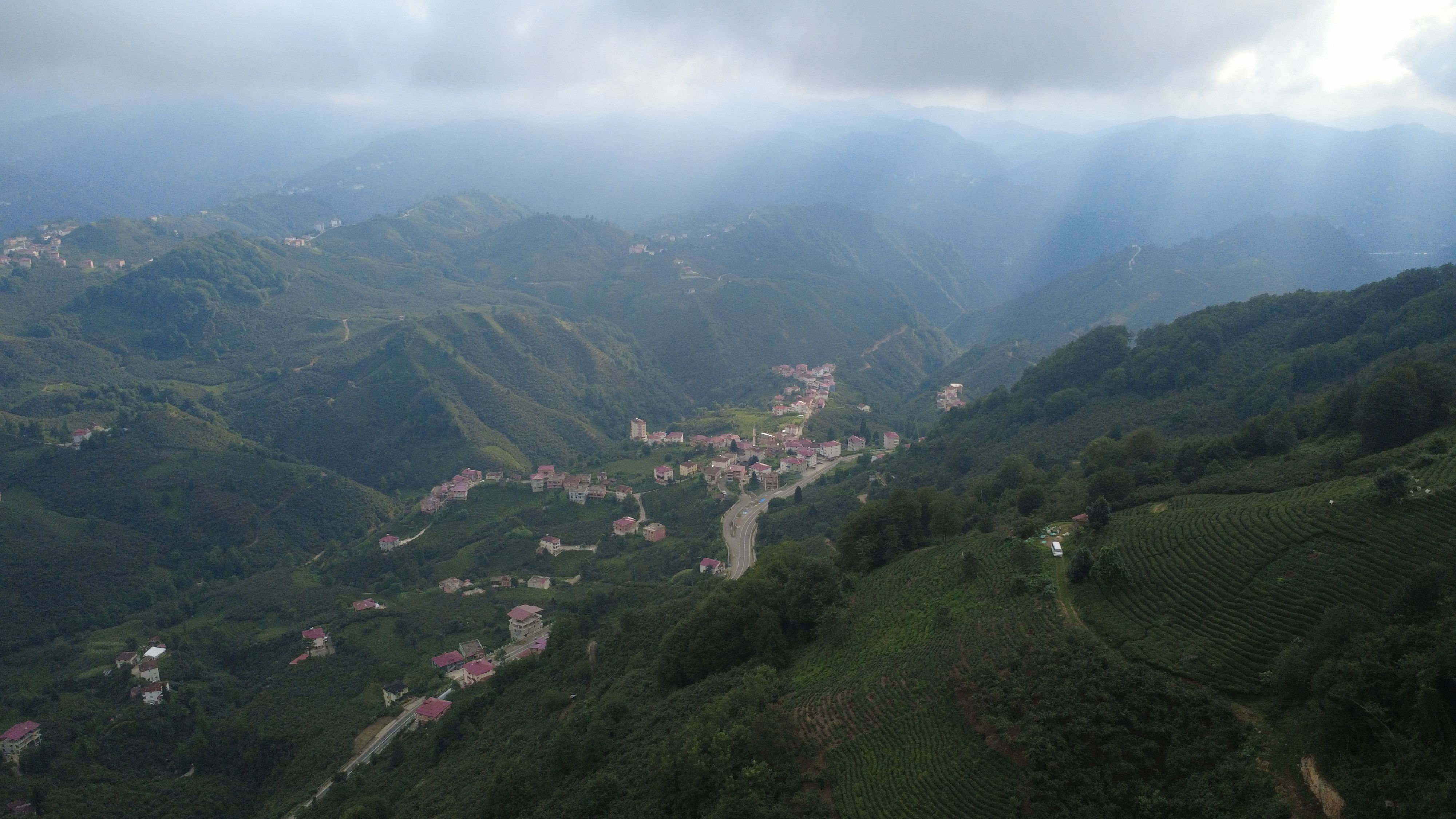A breathtaking aerial view of verdant mountains, valleys, and a quaint village under a cloudy sky.