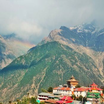 Scenic view of Kalpa with mountains, temples, and a rainbow in the sky.