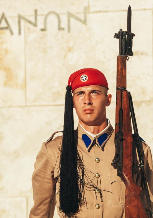 Free Evzone soldier in traditional attire holding a rifle outside a historic monument in Athens. Stock Photo