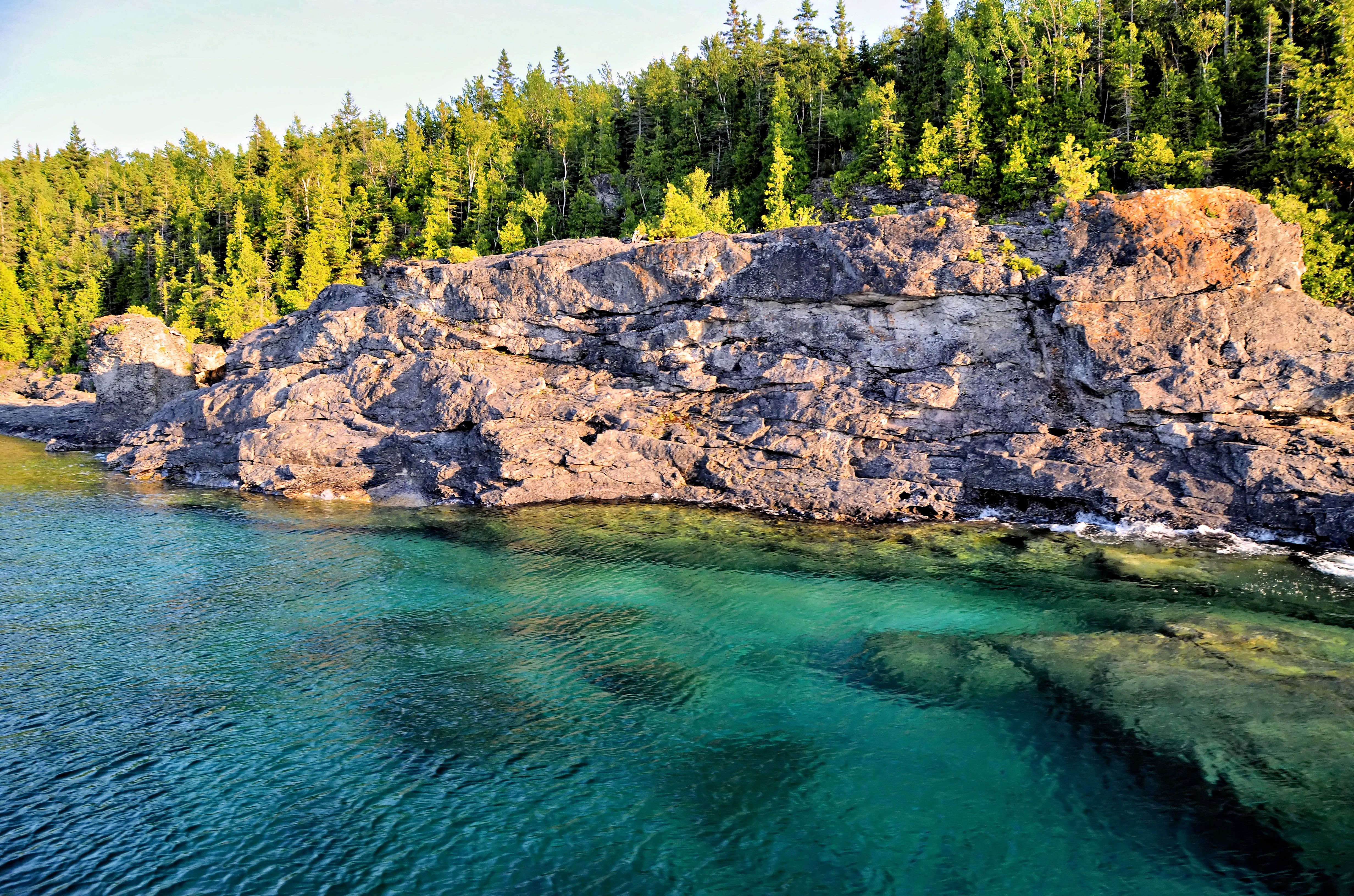 Rocky shoreline and vibrant water at Bruce Peninsula, Ontario, Canada, during daytime.