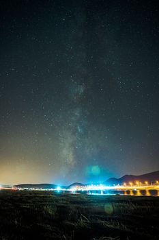 Captivating starry night with Milky Way and a brightly lit bridge reflecting on the water.