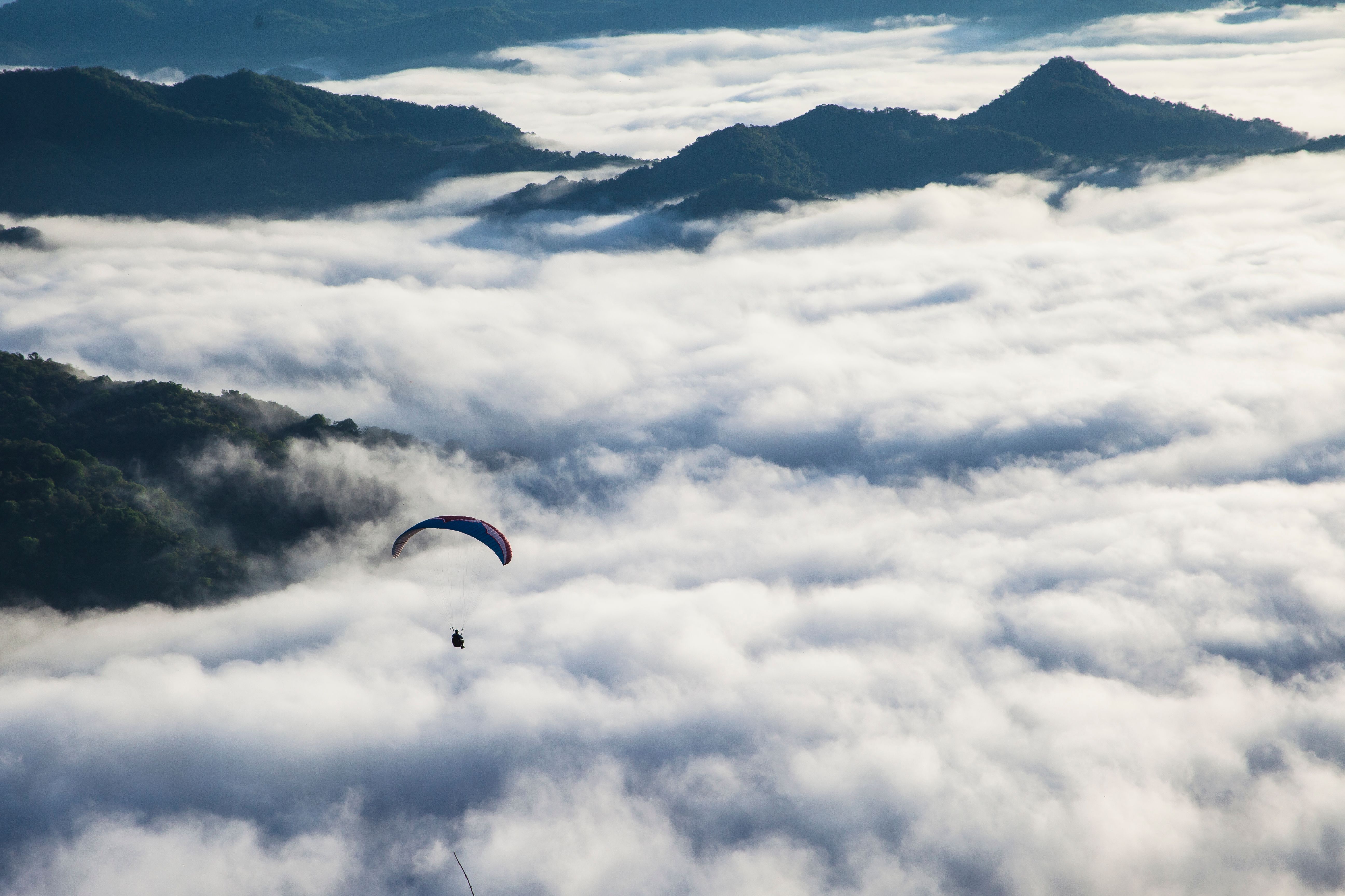 A paraglider floats high above sweeping mountain clouds, capturing a sense of adventure.