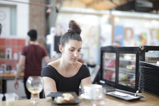 Woman seated at a café counter with hair in a bun, looking focused, surrounded by coffee cups.