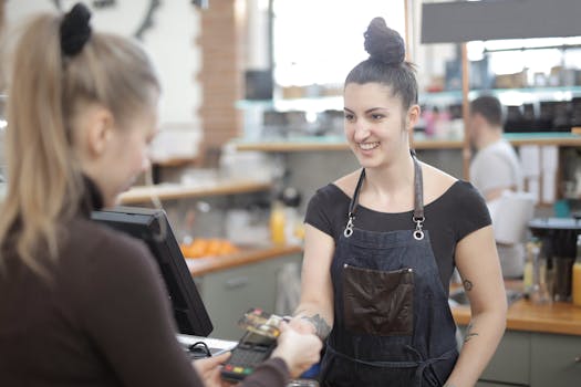 Barista in apron accepting a customer's digital payment in a cozy cafe setting.