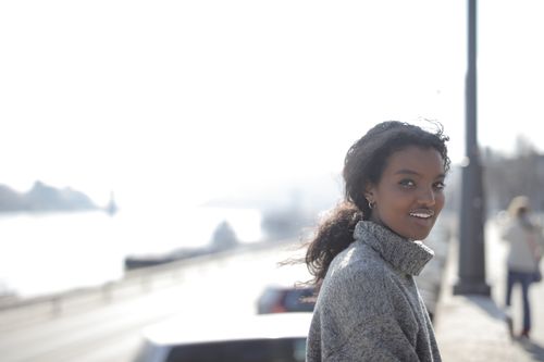 Free Portrait of a smiling woman outdoors in a cozy grey sweater on a bright day. Stock Photo