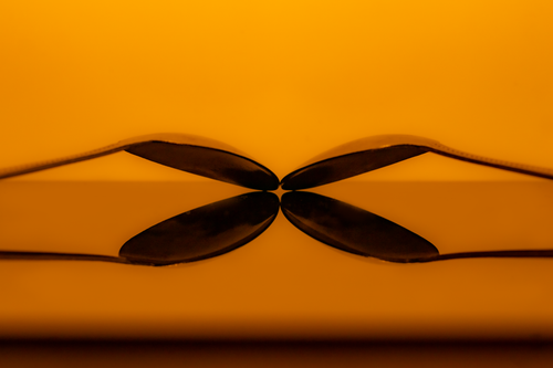 Free Close-up of spoons reflecting symmetrically on a glossy surface, warm orange tone. Stock Photo
