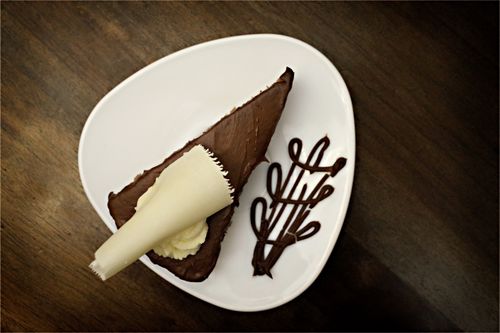 Free A beautiful slice of chocolate cake adorned with white chocolate on a white plate with artistic chocolate decoration. Stock Photo