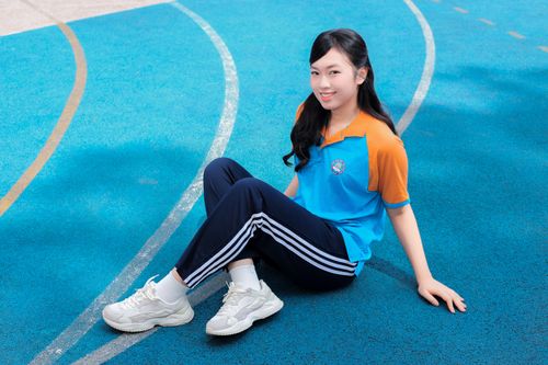 Free Smiling young woman sitting on a vibrant blue track field in Hanoi, Vietnam under the daylight. Stock Photo