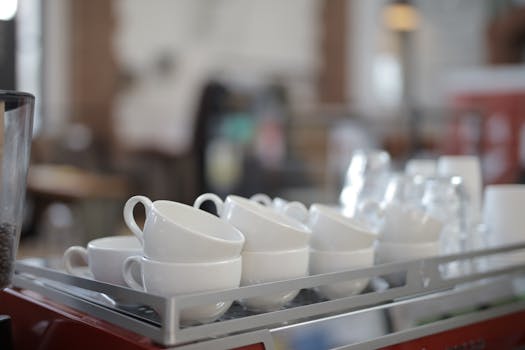 Stack of empty ceramic cups on a coffee machine in a cozy cafe environment.