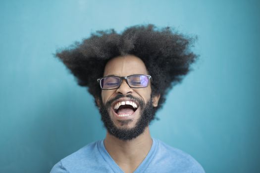 一个快乐的、留着非洲式发型、戴着眼镜的男人在蓝色背景下开怀大笑