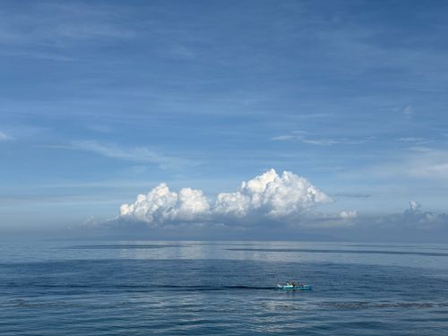 Free A serene ocean view with a small boat under a vast, cloud-filled sky, captured in the Philippines. Stock Photo