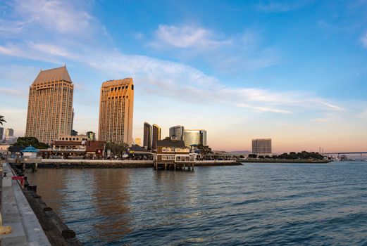 Scenic view of San Diego's waterfront skyline with iconic buildings at sunset, reflecting on calm waters.