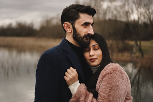 Man in Blue Suit Hugging Woman in Brown Coat