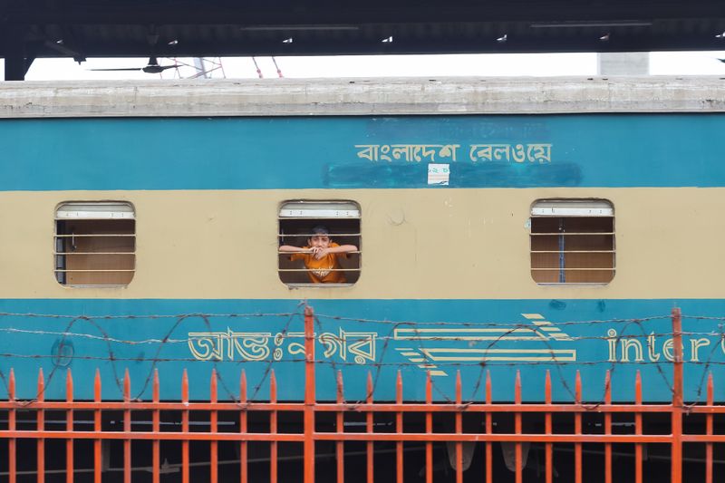 A passenger looks out from a Bangladesh Railways train at a station.