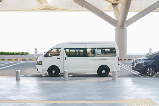 A white minivan parked at a modern airport terminal drop-off zone, ideal for travel and transport concepts.