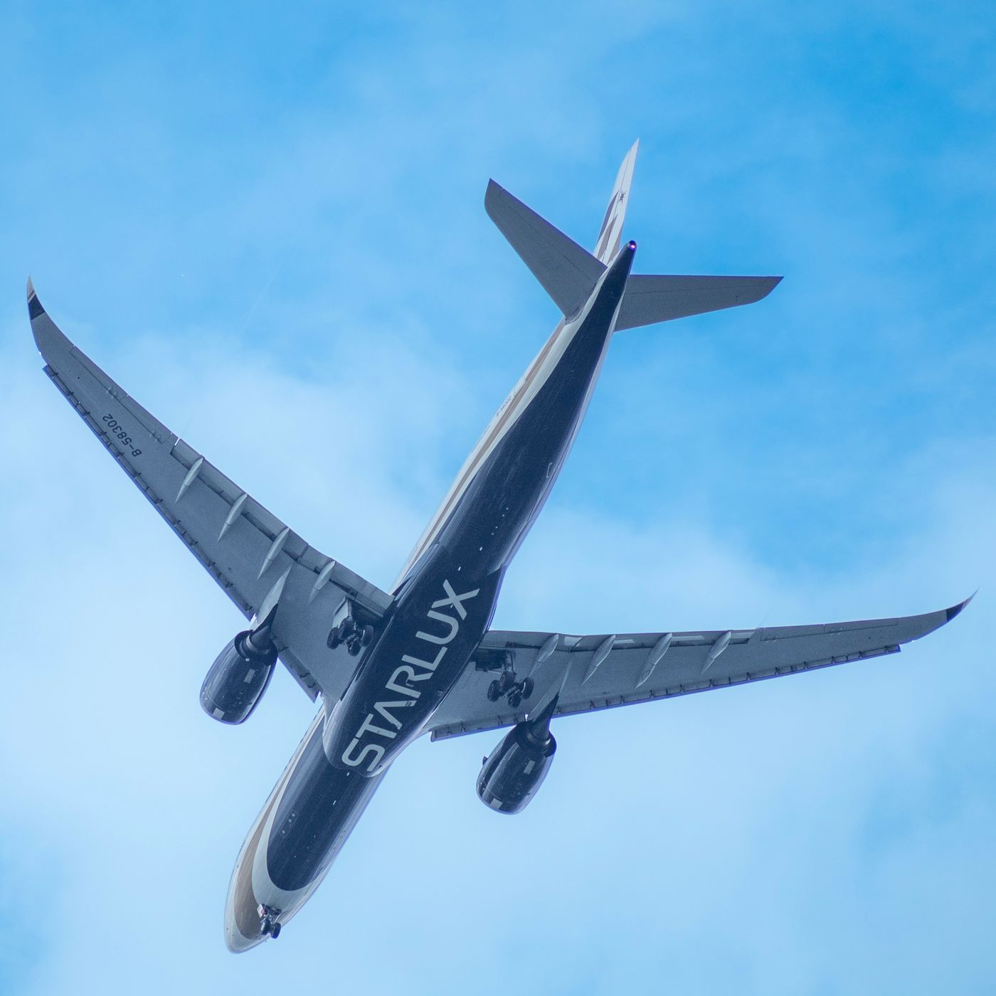 A STARLUX Airlines Airbus A350 photographed from below against a clear blue sky
