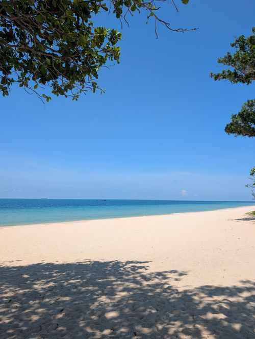 Free Relaxing view of a serene tropical beach with pristine sand, blue sky, and calm sea, perfect for a tranquil escape. Stock Photo
