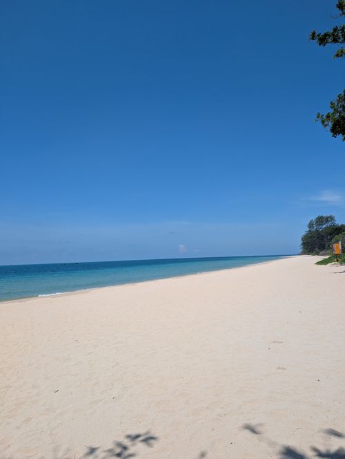 Free A tranquil sandy beach with crystal blue waters and clear skies, ideal for summer relaxation. Stock Photo
