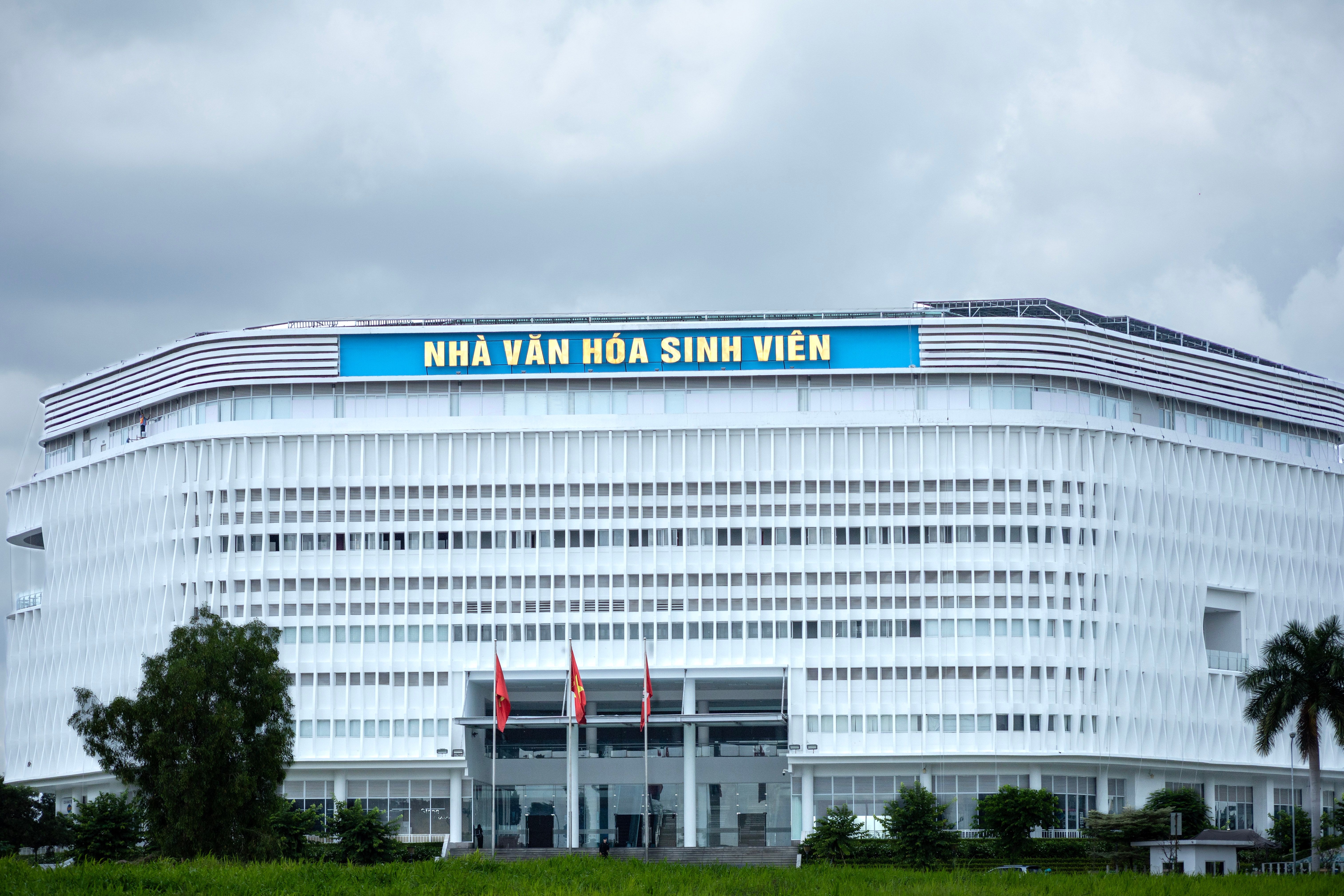 Nhà nghiên cứu ghi chép bên sân đá gà Bali, sổ tay mở cạnh hàng rào tre và lồng gà