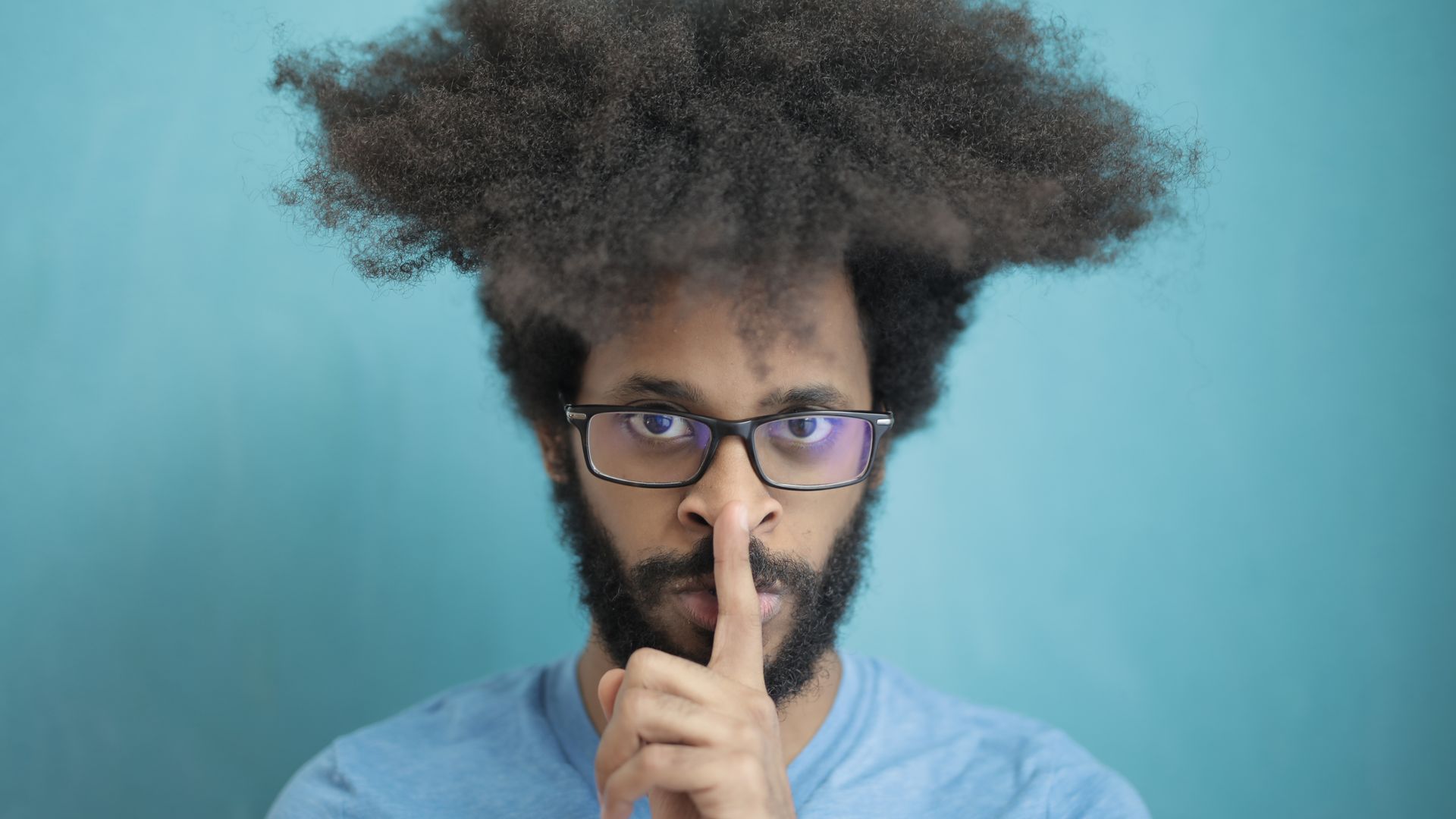 Modafinil Hair Thinning Myth: Unraveling the Truth Man with prominent afro hair making a silence gesture against a blue background — modafinil hair thinning myth